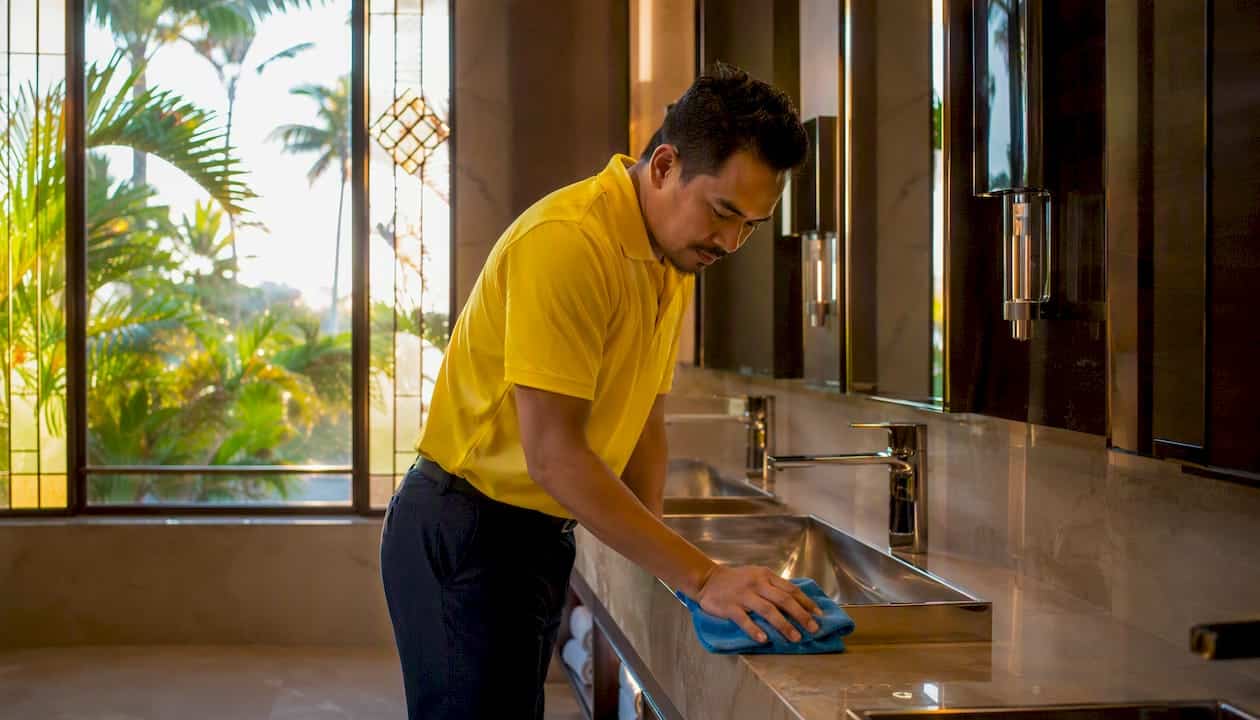 Janitorial staff sanitizing commercial restroom faucet