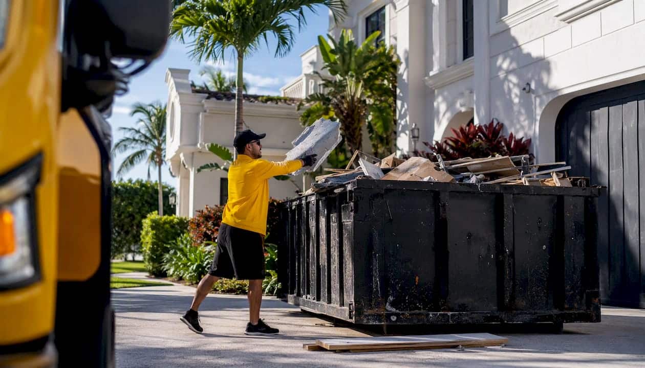 Cleaner loading construction debris into roll-off dumpster