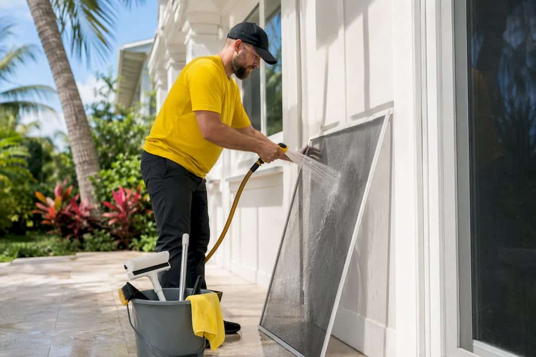 Cleaner leaning a wet window screen to dry outdoors